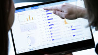 Hand pointing at computer screens with data graphs.